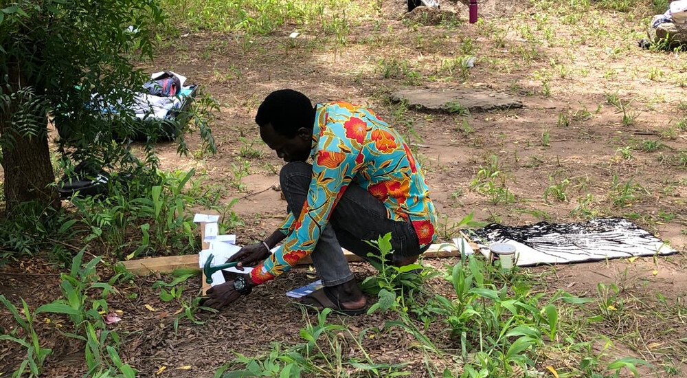 Deltager sidder på jorden og nagler papir fast til trækors. 