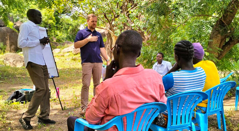 Deltagere sidder med ryggen til i blå plastikstole og kigger mod 2 undervisere. 